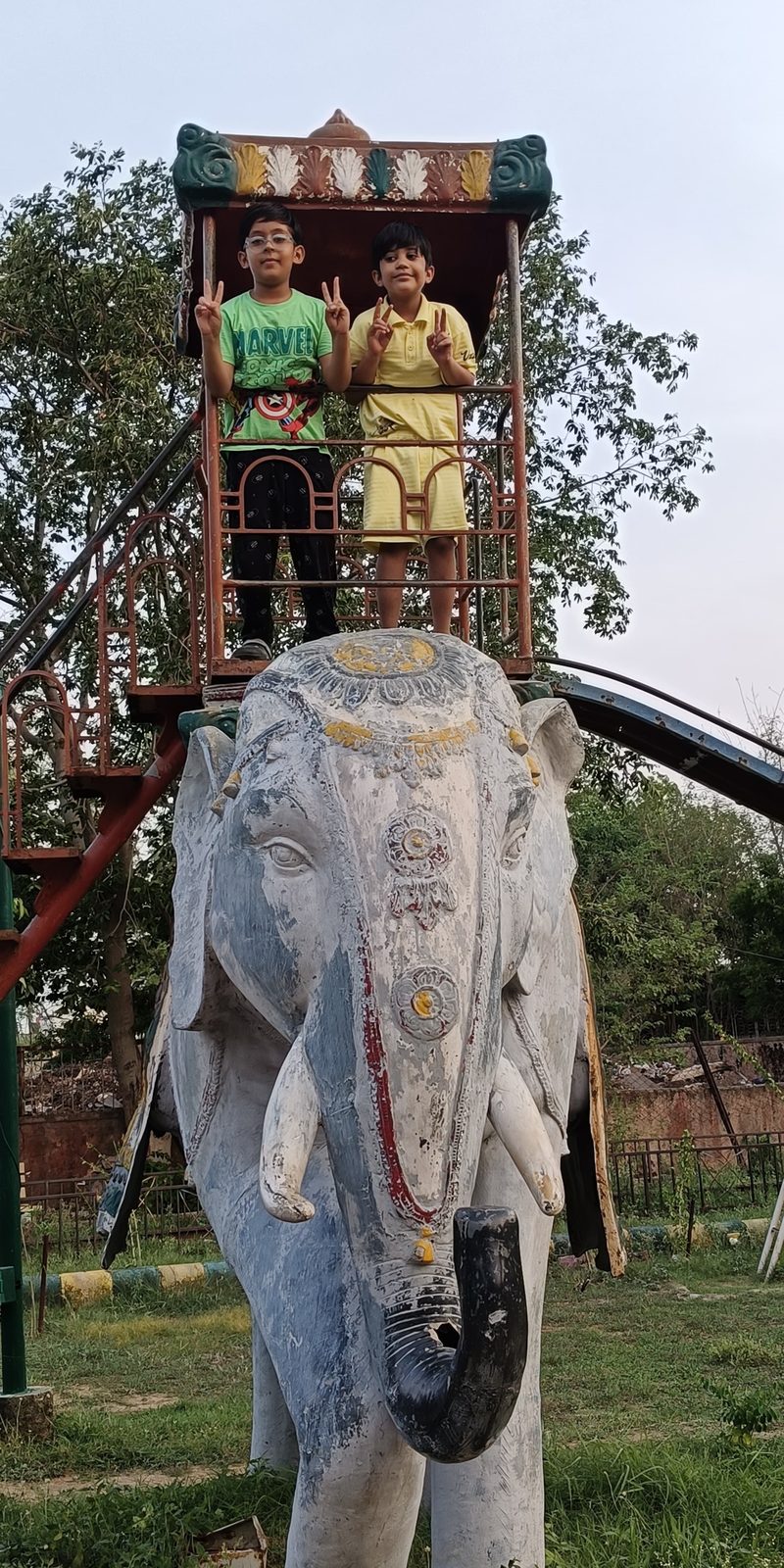Two children playing on an elephant slide at the park